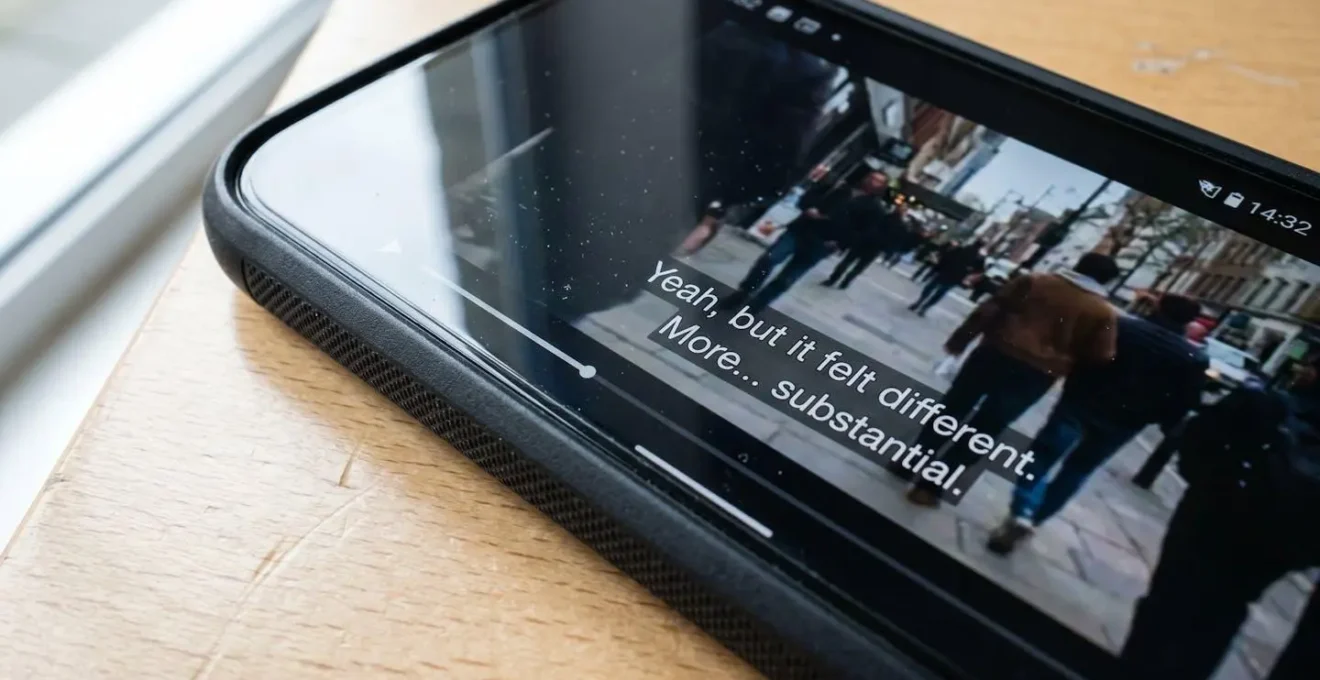 Extreme close-up of a smartphone screen displaying a video player with visible subtitle text overlay, with a finger positioned near the play button