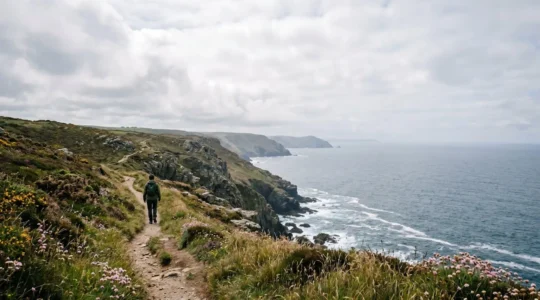 A solitary hiker walking along a dramatic coastal footpath with sweeping views of untouched British coastline under natural light